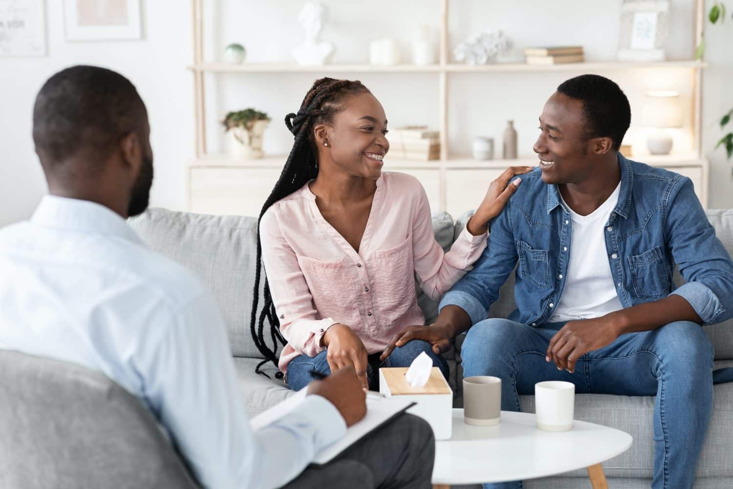 Happy black spouses reconciling after successful family therapy at counselor's office