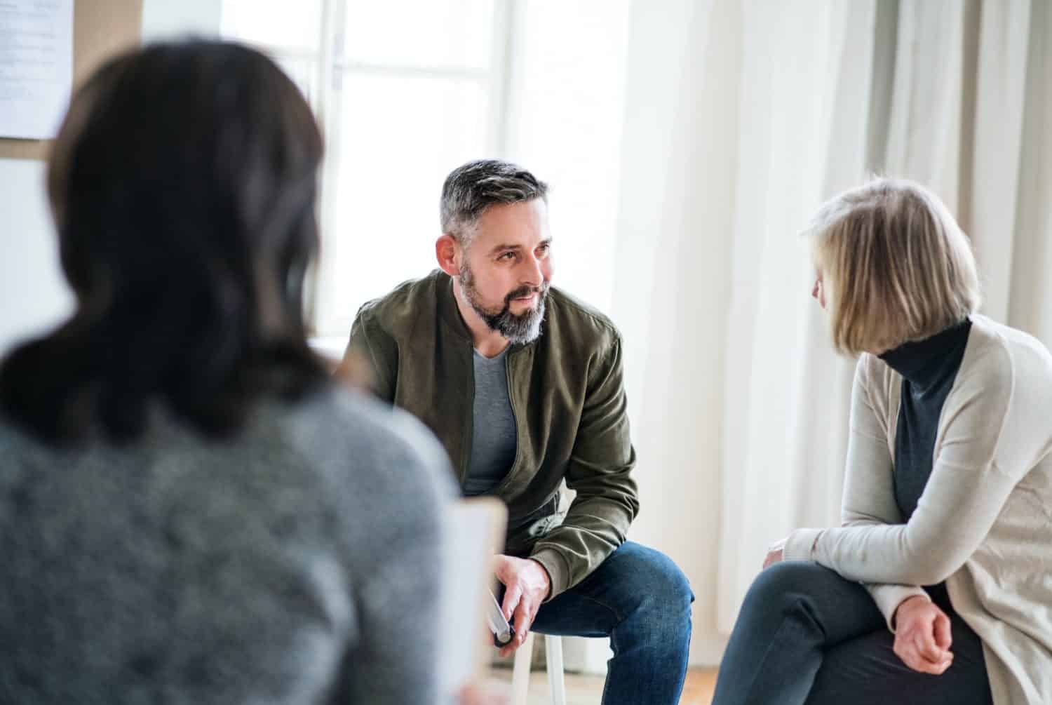 Man and women sitting in a circle during group therapy, talking.