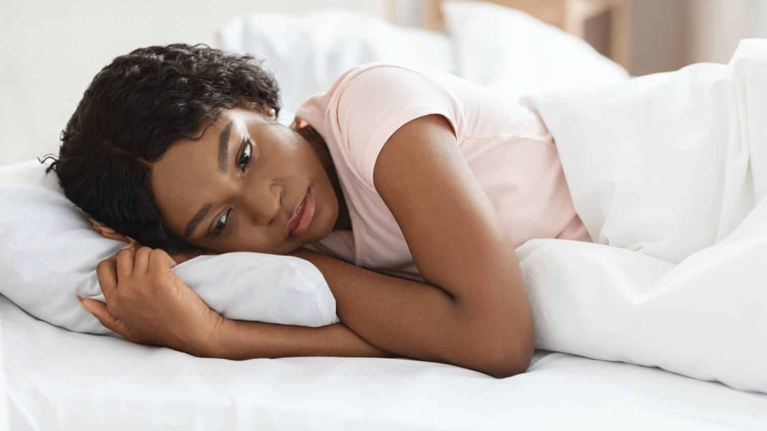 Depressed black woman laying alone in bed