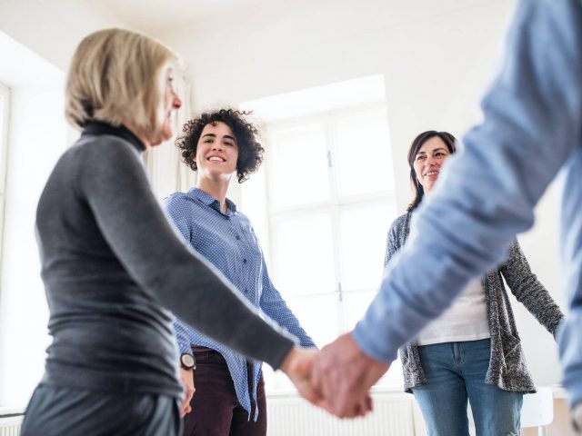 Group of people standing in a circle and holding hands during therapy.